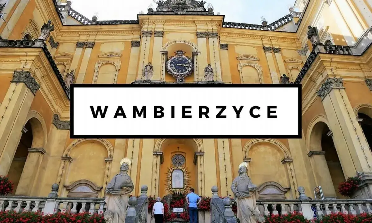 Wambierzyce atrakcje: imponująca bazylika z zegarem i rzeźbami, otoczona kwitnącymi czerwonymi kwiatami.
