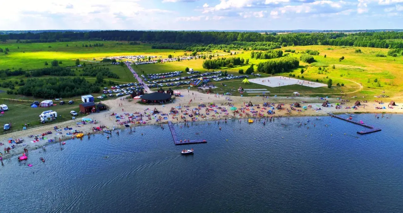Tłoczna plaża nad jeziorem na Dolnym Śląsku, z ludźmi opalającymi się, pływającymi i bawiącymi się.