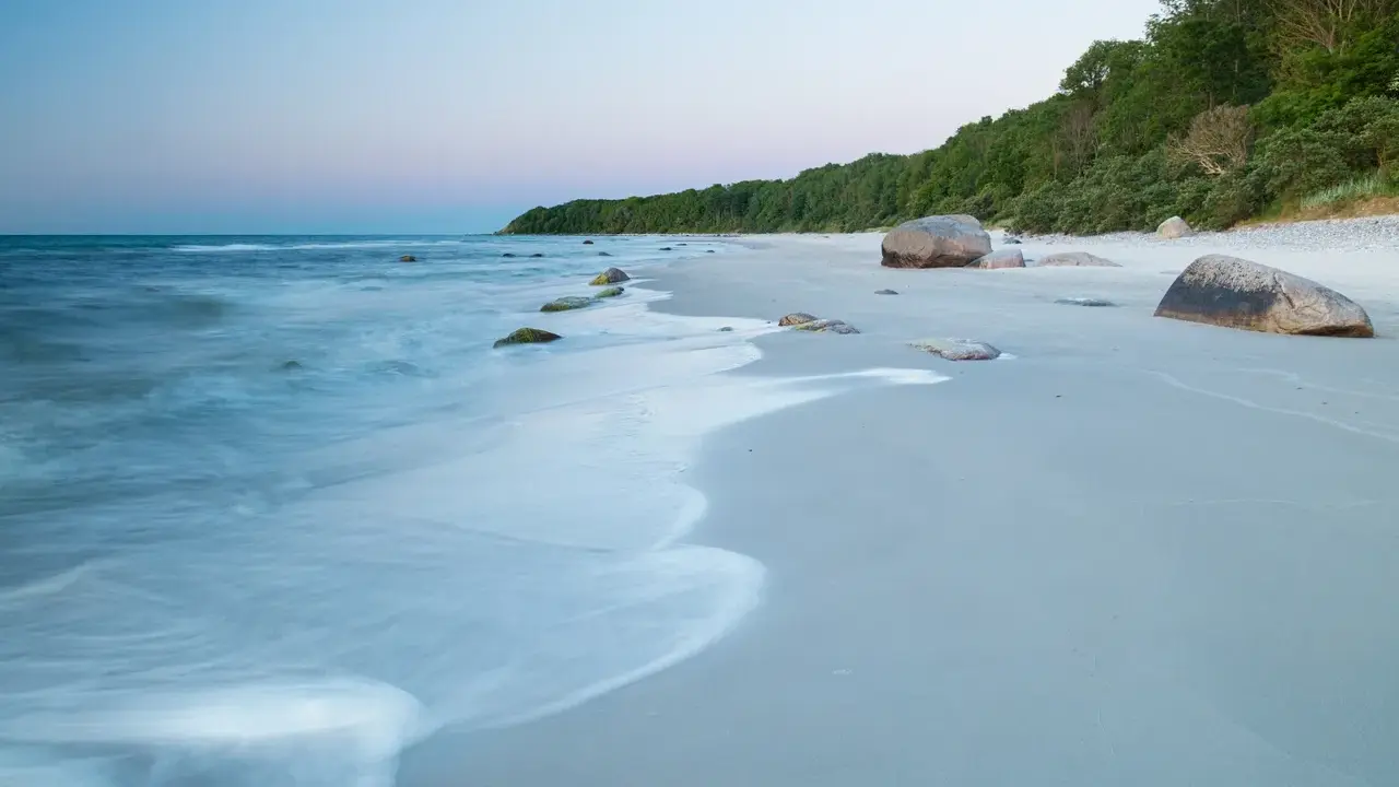 Spokojne plaże nad morzem o świcie, z delikatnymi falami obmywającymi kamienie i piaszczysty brzeg.