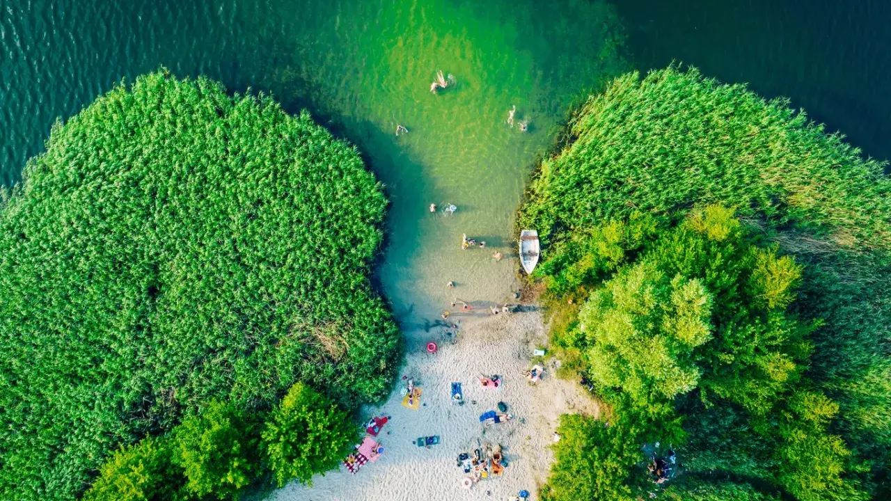 Letnie słońce ogrzewa plażowiczów nad jednym z najpiękniejszych jezior w Polsce. Woda kusi kąpiących się, a łódka czeka przy brzegu.