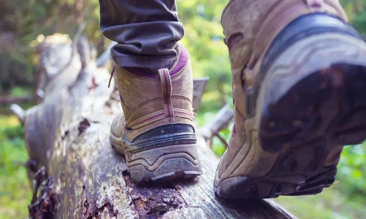 Osoba w butach trekkingowych stąpa po powalonym drzewie. Czy buty trekkingowe powinny być większe? Zapewniają stabilność na nierównym terenie.