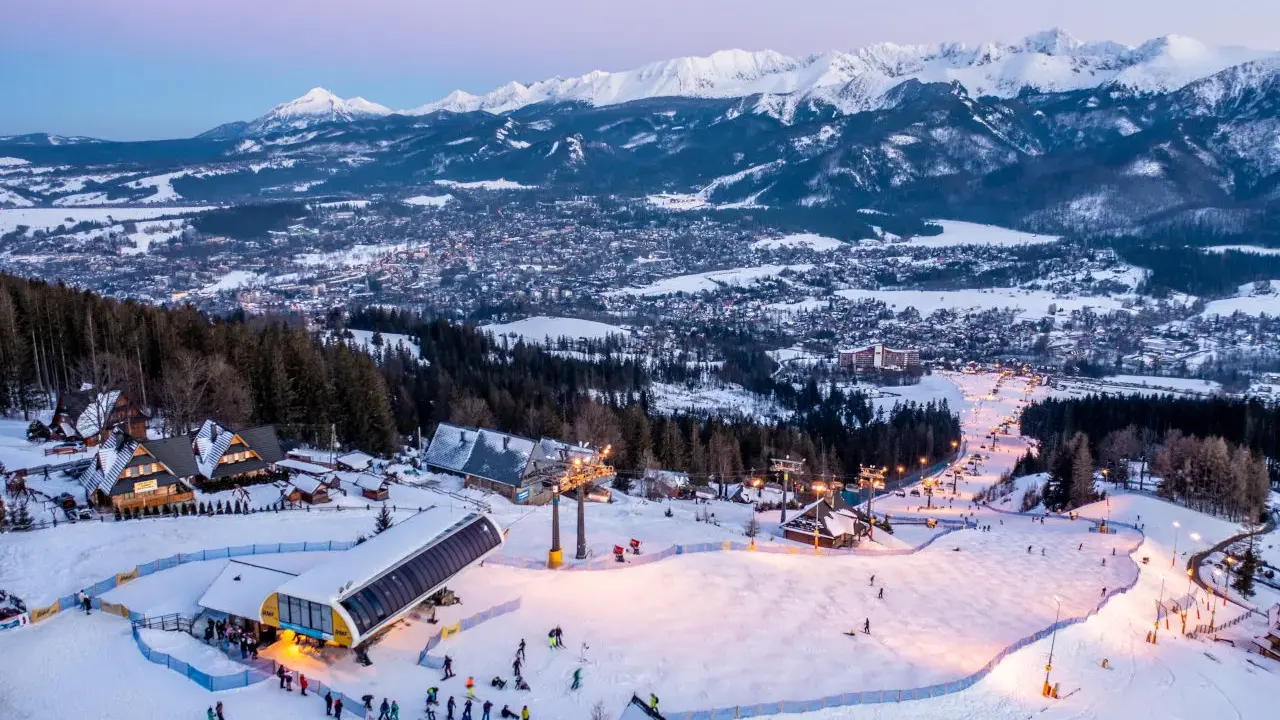 Ośnieżone stoki i kolejka na Kasprowy Wierch to jedne z wielu zakopiańskich atrakcji. W tle widać panoramę miasta i Tatry.