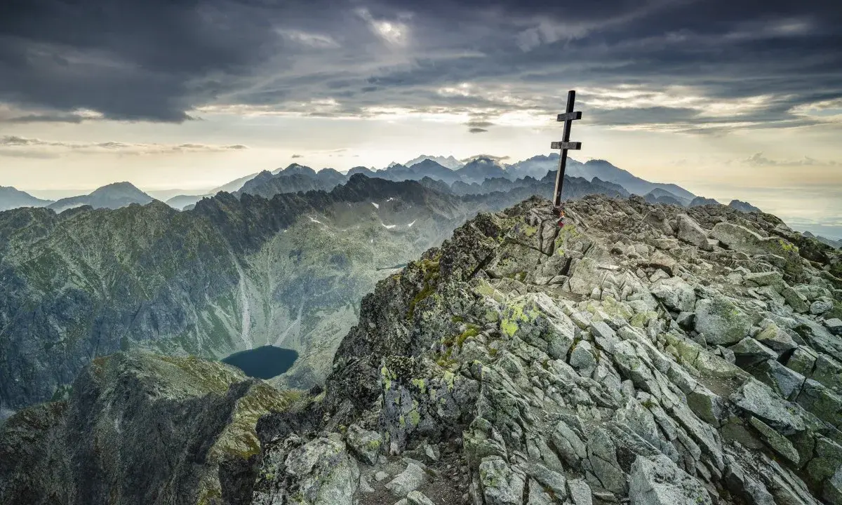 Kamienisty szczyt z krzyżem, widok na Tatry i jezioro. Krywań szlak w chmurach.