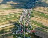 Długa wieś w Polsce, rozciągająca się wzdłuż drogi, otoczona polami o różnych kolorach.