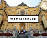 Wambierzyce atrakcje: imponująca bazylika z zegarem i rzeźbami, otoczona kwitnącymi czerwonymi kwiatami.