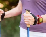 Dłonie trzymające kijki do nordic walking, z czerwonym zegarkiem na nadgarstku. To świetny sposób, jak chodzić z kijkami, by wzmocnić ciało.