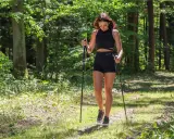 Młoda kobieta w czarnym sportowym stroju uprawia sport z kijami w lesie.