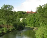 Zielona dolina Nysy Kłodzkiej w Bardo Śląskim. Rzeka meandruje wśród bujnej roślinności, a na wzgórzu majaczy klasztor.