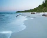 Spokojne plaże nad morzem o świcie, z delikatnymi falami obmywającymi kamienie i piaszczysty brzeg.