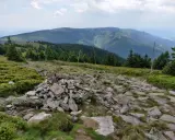 Kamienista ścieżka prowadzi przez zielone wzgórza w kierunku gór. Widok na pasmo górskie w oddali, przypominające krajobraz w okolicach Bystrzycy Kłodzkiej.