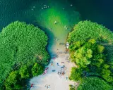 Letnie słońce ogrzewa plażowiczów nad jednym z najpiękniejszych jezior w Polsce. Woda kusi kąpiących się, a łódka czeka przy brzegu.