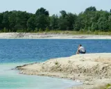 Samotny mężczyzna siedzi na brzegu, kontemplując turkusową wodę. To spokojne miejsce, jakby zapomniany osadnik gajówka.