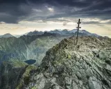 Kamienisty szczyt z krzyżem, widok na Tatry i jezioro. Krywań szlak w chmurach.