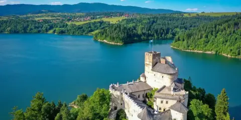Zamek w Niedzicy góruje nad turkusowym jeziorem Czorsztyńskim, otoczony zielonymi lasami i pagórkami.