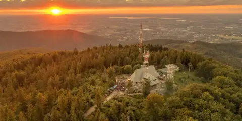 Zachód słońca nad lasem i budynkami na szczycie. Ludzie spacerują po szlakach na Szyndzielni.