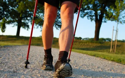 Nogi w butach do nordic walking, z kijkami w rękach, na ścieżce. Dowiedz się, jak prawidłowo założyć buciki na kijki nordic walking.