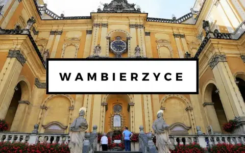 Wambierzyce atrakcje: imponująca bazylika z zegarem i rzeźbami, otoczona kwitnącymi czerwonymi kwiatami.