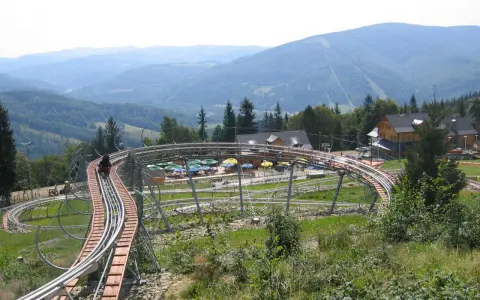 Zjazd kolejką górską w Ustroniu, z widokiem na Beskidy. W tle góry i lasy.
