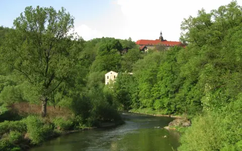Zielona dolina Nysy Kłodzkiej w Bardo Śląskim. Rzeka meandruje wśród bujnej roślinności, a na wzgórzu majaczy klasztor.