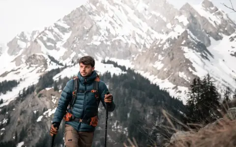 Mężczyzna w kurtce z ociepliną **Primaloft Gold** wędruje po górskim szlaku, wspierając się kijkami.