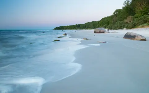 Spokojne plaże nad morzem o świcie, z delikatnymi falami obmywającymi kamienie i piaszczysty brzeg.