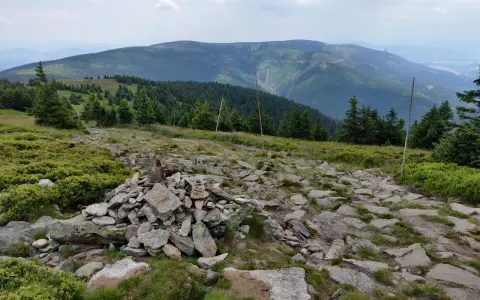 Kamienista ścieżka prowadzi przez zielone wzgórza w kierunku gór. Widok na pasmo górskie w oddali, przypominające krajobraz w okolicach Bystrzycy Kłodzkiej.