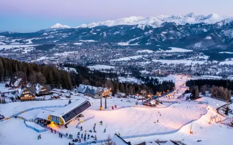 Ośnieżone stoki i kolejka na Kasprowy Wierch to jedne z wielu zakopiańskich atrakcji. W tle widać panoramę miasta i Tatry.