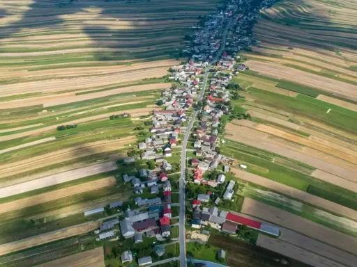 Długa wieś w Polsce, rozciągająca się wzdłuż drogi, otoczona polami o różnych kolorach.
