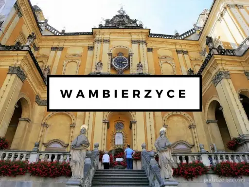 Wambierzyce atrakcje: imponująca bazylika z zegarem i rzeźbami, otoczona kwitnącymi czerwonymi kwiatami.
