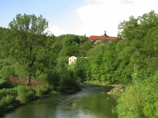 Zielona dolina Nysy Kłodzkiej w Bardo Śląskim. Rzeka meandruje wśród bujnej roślinności, a na wzgórzu majaczy klasztor.
