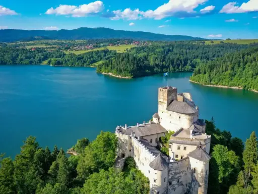Zamek w Niedzicy góruje nad turkusowym jeziorem Czorsztyńskim, otoczony zielonymi lasami i pagórkami.