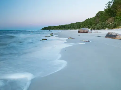 Spokojne plaże nad morzem o świcie, z delikatnymi falami obmywającymi kamienie i piaszczysty brzeg.