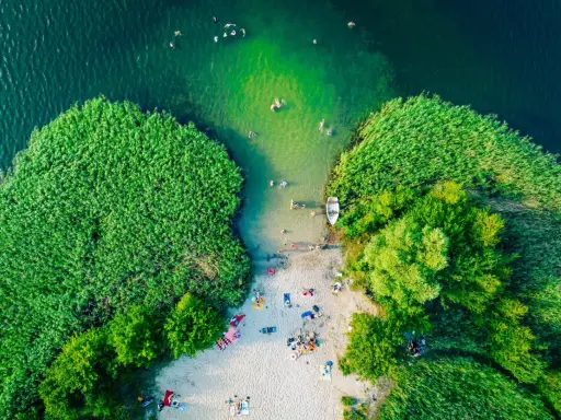 Letnie słońce ogrzewa plażowiczów nad jednym z najpiękniejszych jezior w Polsce. Woda kusi kąpiących się, a łódka czeka przy brzegu.