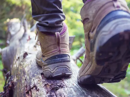 Osoba w butach trekkingowych stąpa po powalonym drzewie. Czy buty trekkingowe powinny być większe? Zapewniają stabilność na nierównym terenie.