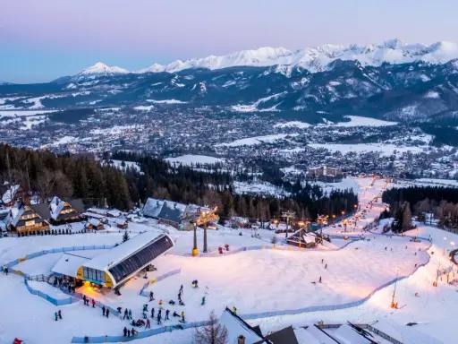 Ośnieżone stoki i kolejka na Kasprowy Wierch to jedne z wielu zakopiańskich atrakcji. W tle widać panoramę miasta i Tatry.