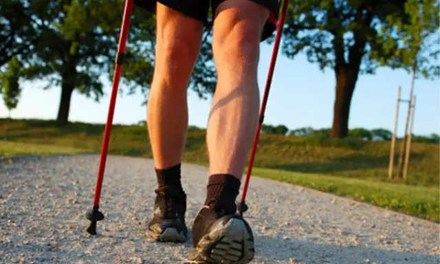 Nogi w butach do nordic walking, z kijkami w rękach, na ścieżce. Dowiedz się, jak prawidłowo założyć buciki na kijki nordic walking.