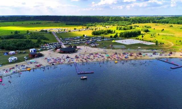 Tłoczna plaża nad jeziorem na Dolnym Śląsku, z ludźmi opalającymi się, pływającymi i bawiącymi się.