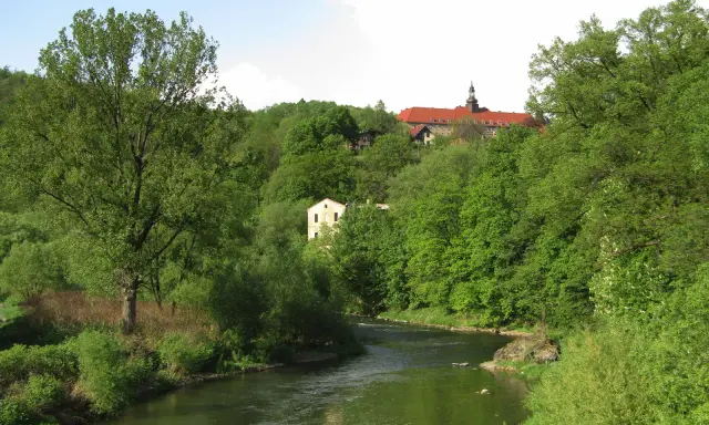 Zielona dolina Nysy Kłodzkiej w Bardo Śląskim. Rzeka meandruje wśród bujnej roślinności, a na wzgórzu majaczy klasztor.