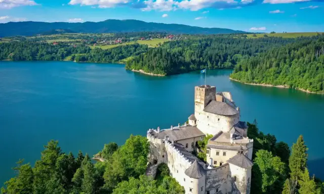 Zamek w Niedzicy góruje nad turkusowym jeziorem Czorsztyńskim, otoczony zielonymi lasami i pagórkami.
