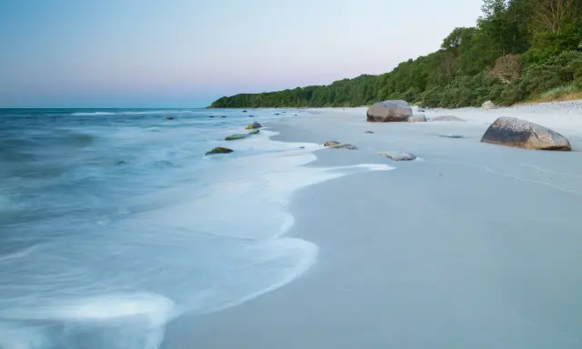 Spokojne plaże nad morzem o świcie, z delikatnymi falami obmywającymi kamienie i piaszczysty brzeg.