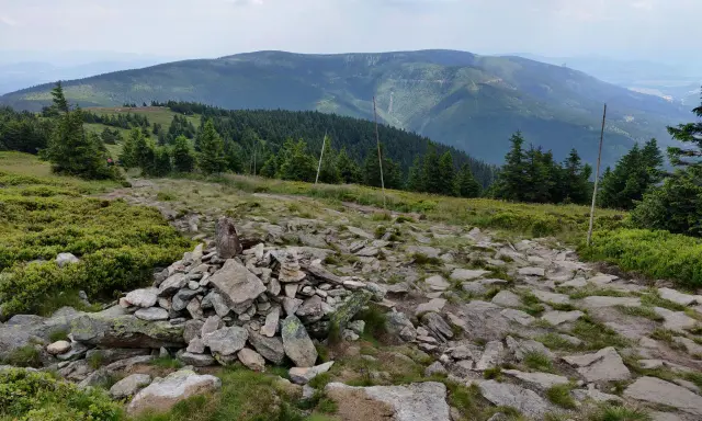 Kamienista ścieżka prowadzi przez zielone wzgórza w kierunku gór. Widok na pasmo górskie w oddali, przypominające krajobraz w okolicach Bystrzycy Kłodzkiej.