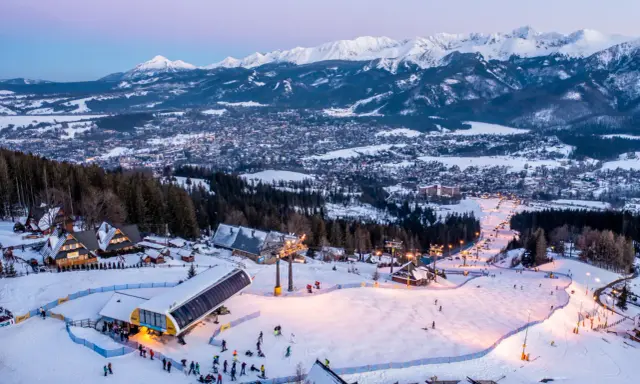 Ośnieżone stoki i kolejka na Kasprowy Wierch to jedne z wielu zakopiańskich atrakcji. W tle widać panoramę miasta i Tatry.