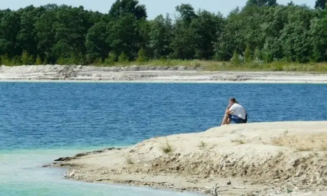 Samotny mężczyzna siedzi na brzegu, kontemplując turkusową wodę. To spokojne miejsce, jakby zapomniany osadnik gajówka.