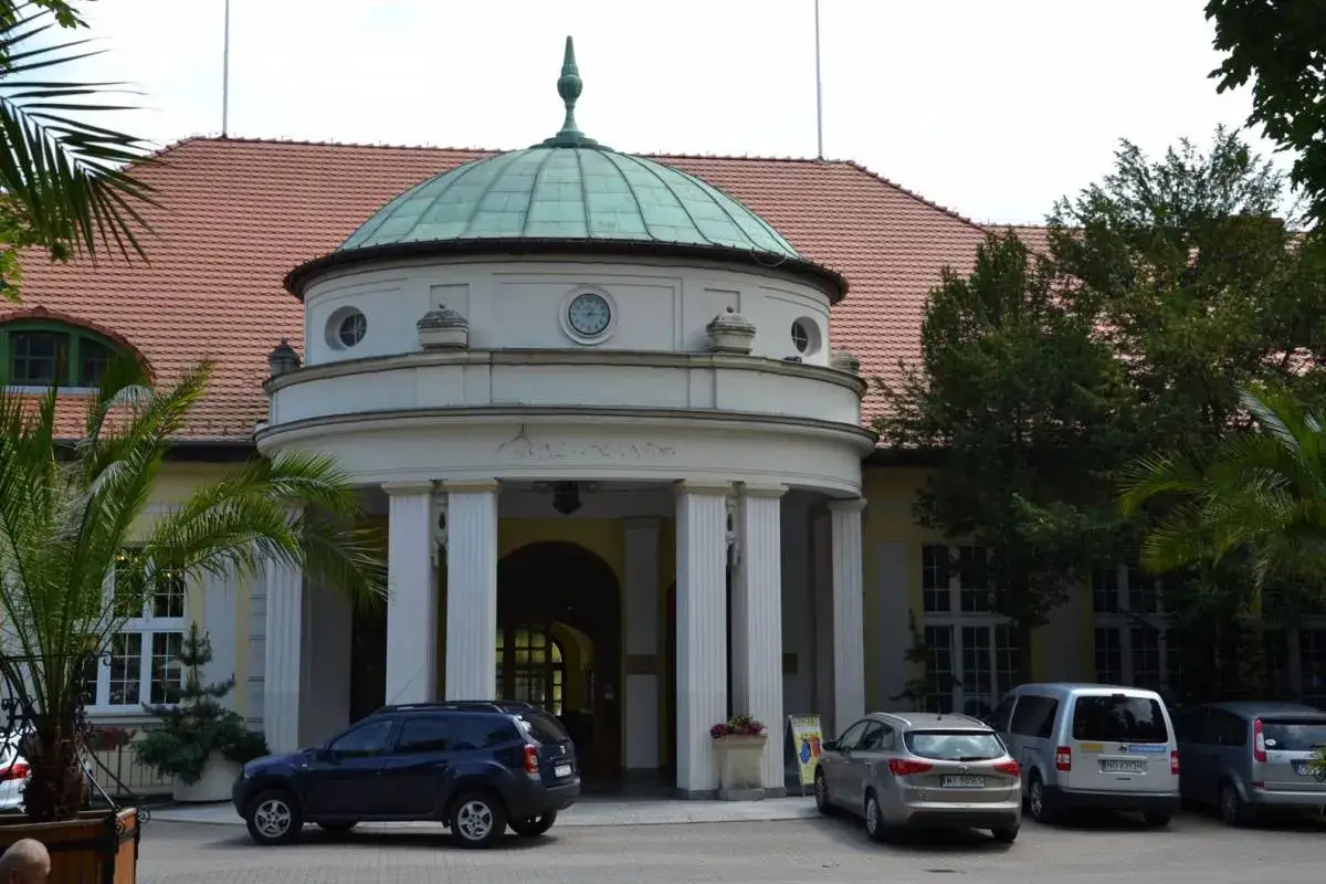 Elegancki budynek z kopułą w Polanicy Zdrój, przed którym stoją samochody.