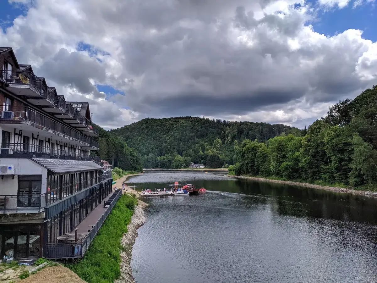 Malownicze jeziora na Śląsku. Hotel nad wodą, z którego roztacza się widok na zalesione wzgórza i spokojną taflę jeziora.
