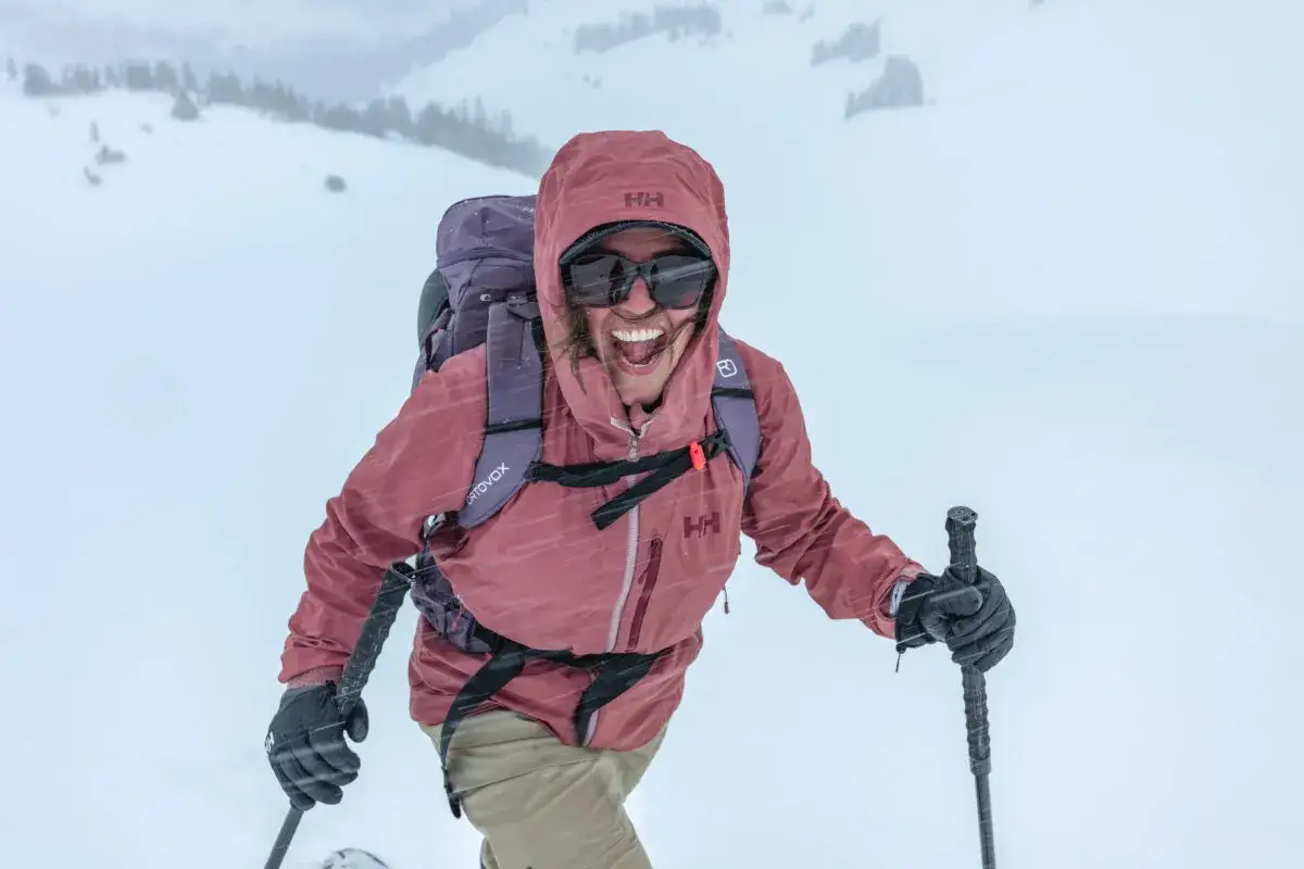 Szczęśliwa narciarka w kurtce Helly Hansen, firmy znanej z odzieży outdoorowej, przemierza ośnieżone stoki.