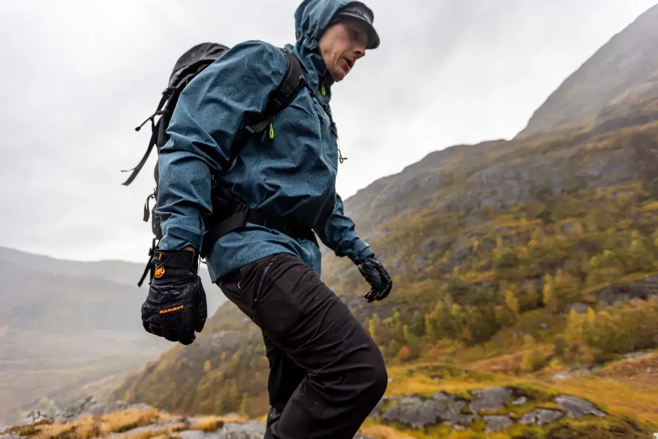 Turysta w deszczu, w kurtce z materiału texapore, który chroni jak gore-tex, przemierza górski szlak.
