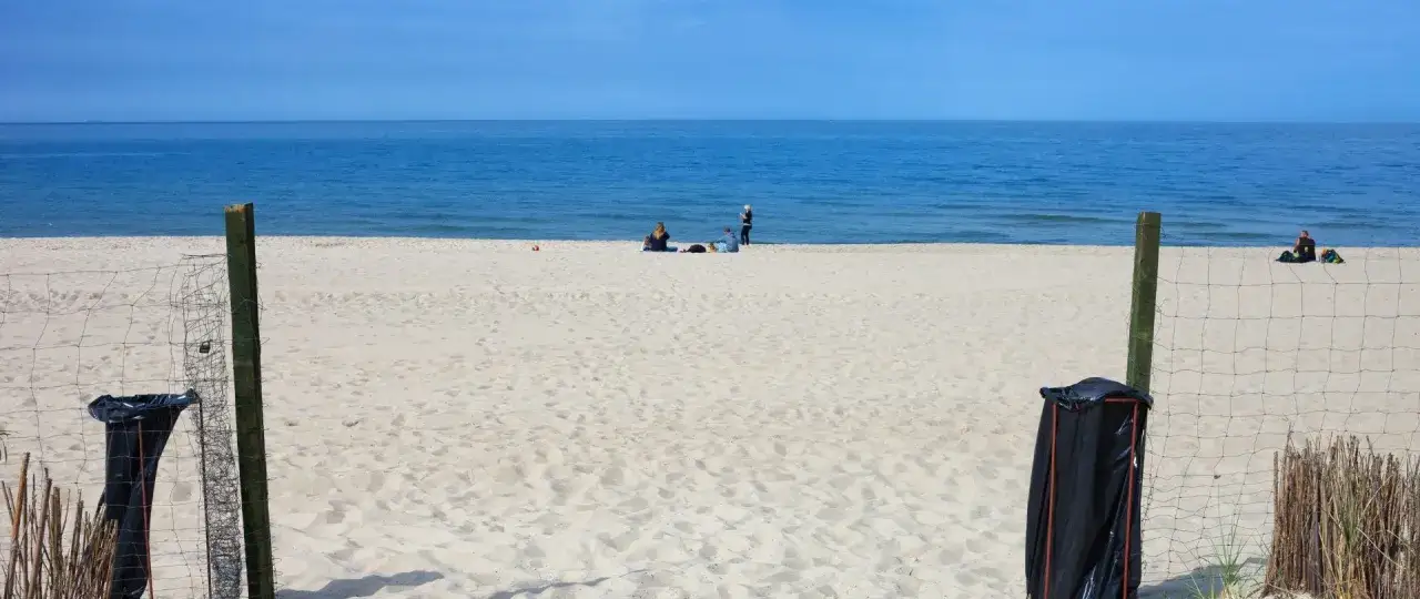 Plaża we Władysławowie, idealne miejsce na wypoczynek. W tle widać morze i kilka os&oacute;b relaksujących się na piasku. Władysławowo atrakcje dla dzieci to przede wszystkim bezpieczne kąpiele i zabawy na piasku.