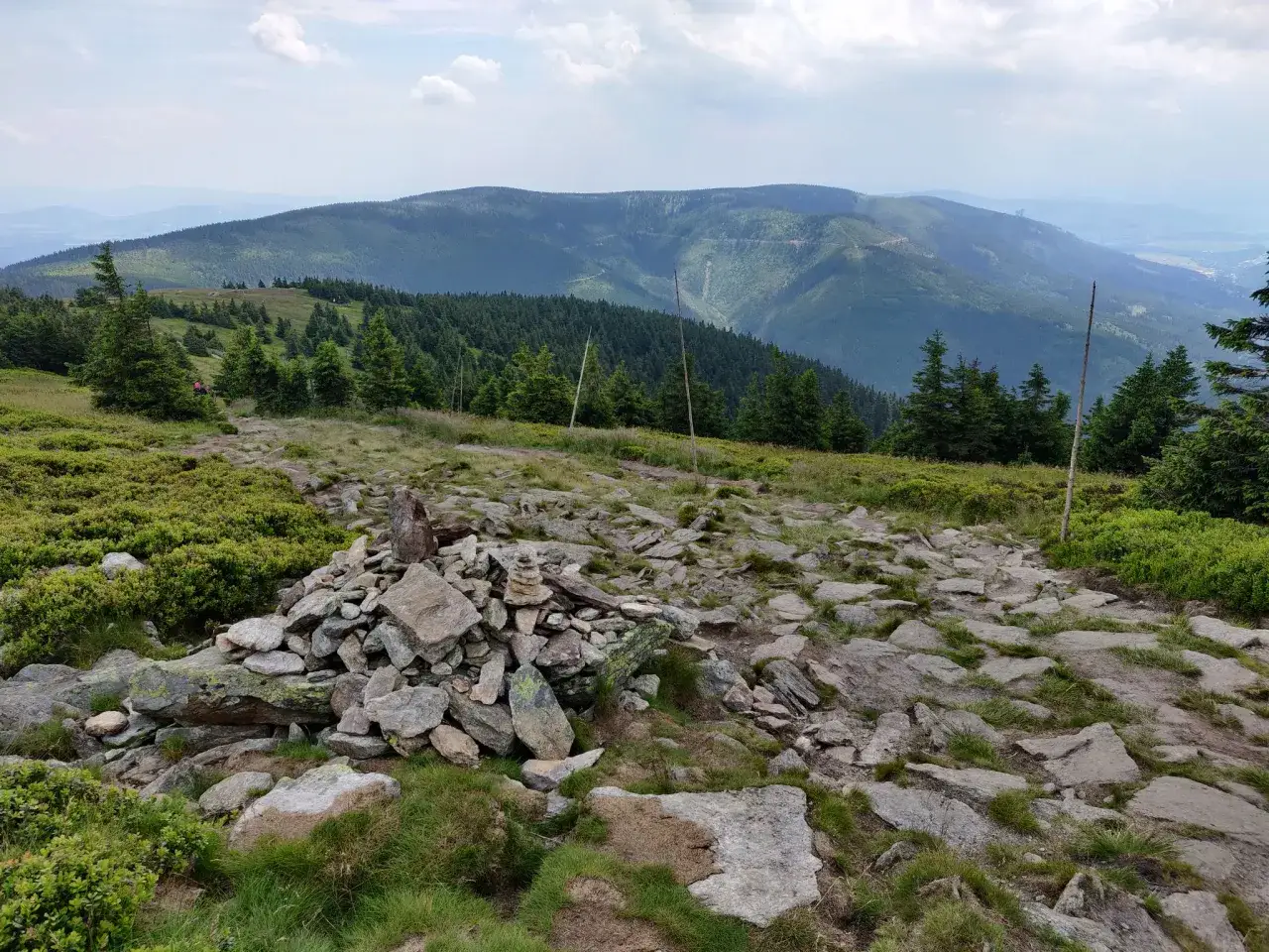 Kamienista ścieżka w górach, widok na pasmo górskie w oddali. Bystrzyca Kłodzka w tle.